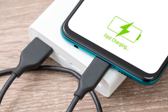Powerbank charging smartphone battery on the table, close up picture. Fast charge, modern technologies, hi-tech devices