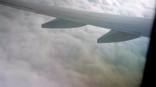 View of airplane wing from inside flying through white puffy clouds
