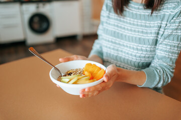 Healthy breakfast bowl with muesli and fruits in woman hands at home. Clean eating, vegetarian,...