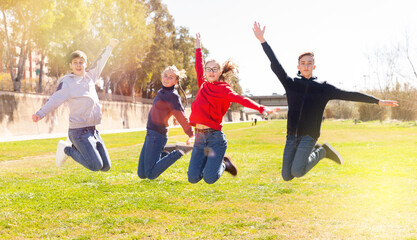 Group of teenagers having fun together outdoors, jumping on green lawn in springtime