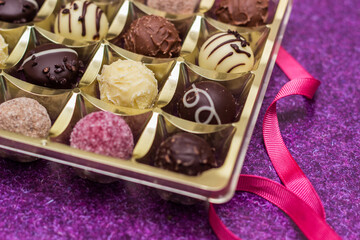 Golden box with delicious chocolate candies on purple table