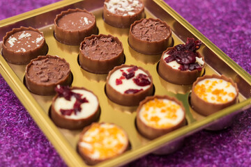 Golden box with delicious chocolate candies on purple table