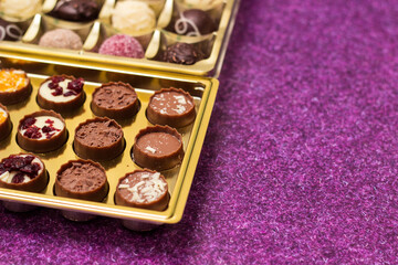 Golden box with delicious chocolate candies on purple table