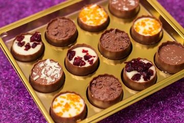 Golden box with delicious chocolate candies on purple table