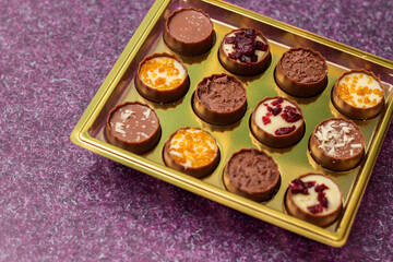 Golden box with delicious chocolate candies on purple table