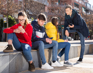 Obraz na płótnie Canvas Portrait of modern teenagers hanging out on streets of city on warm spring day, using phones and chatting