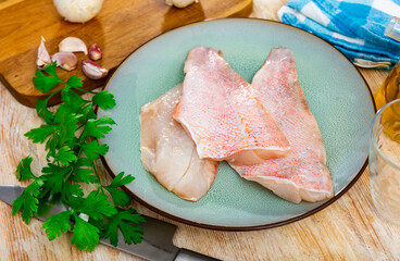 Three pieces of raw sea bass fillet on a plate while cooking in a home kitchen with a sprig of...