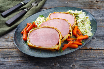 Backed Kasseler pork steak in pastry crust with savoy cabbage and carrots served as close-up on a...