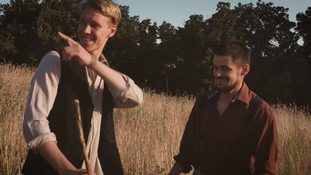 Old adult friends wear vintage clothing in ancient times walking and huging on yellow fields and beautiful views village. Retro style, happy sunny day in village