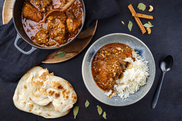 Traditional spicy Indian chicken Madras curry Rogan Josh with chicken, chapati bread and basmati rice served as top view in a saucepan and a Nordic design bowl