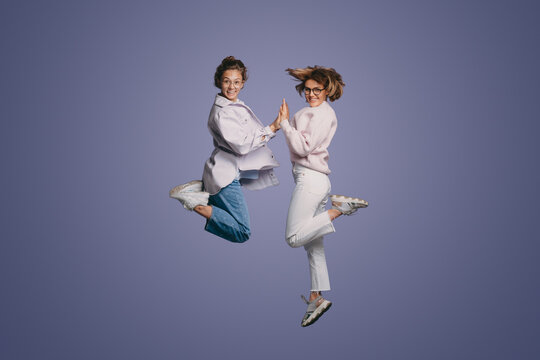 Young cute excited funny smiling women wearing casual clothes jumping up in air and high five clapping hands with joy isolated over purple background.