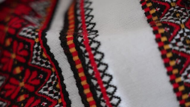Closeup view 4k video of traditional ukrainian embroidery design made with black, red, white and orange yarn on white cotton fabric texture. Embroidery pattern background. Focus slides back and force