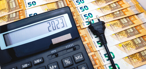 Calculator, electric plug, 50 euro notes and coins in the background. The concept of the high cost of electricity, rising inflation and the impending crisis in 2023 - obrazy, fototapety, plakaty