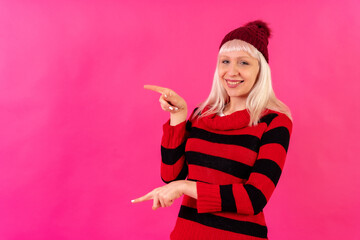 Obraz na płótnie Canvas Blonde caucasian girl on pink background studio, winter theme, smiling pointing left