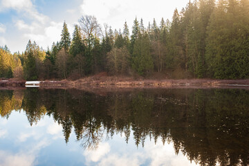 Autumn morning in the forest with lake, forest reflection and mist on the water surface.