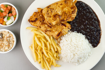 Delicious executive dish of chicken fillet, rice, beans, french fries and green salad with lettuce, tomato and onion accompanied by farofa and vinaigrette. Typical Brazilian food. Selective focus