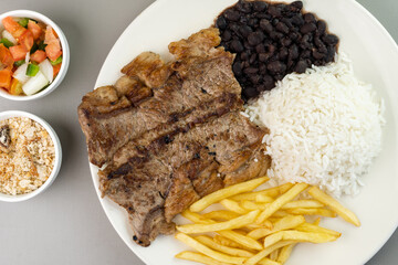 Delicious executive dish of beef steak, rice, beans, french fries and green salad with lettuce, tomato and onion accompanied by farofa and vinaigrette. Typical Brazilian food. Selective focus