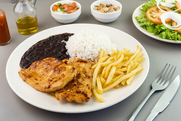 Delicious executive dish of chicken fillet, rice, beans, french fries and green salad with lettuce, tomato and onion accompanied by farofa and vinaigrette. Typical Brazilian food. Selective focus