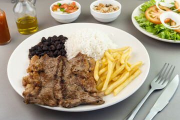 Delicious executive dish of beef steak, rice, beans, french fries and green salad with lettuce, tomato and onion accompanied by farofa and vinaigrette. Typical Brazilian food. Selective focus