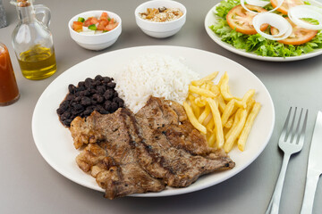 Delicious executive dish of beef steak, rice, beans, french fries and green salad with lettuce, tomato and onion accompanied by farofa and vinaigrette. Typical Brazilian food. Selective focus