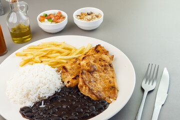 Delicious executive dish of chicken fillet, rice, beans, french fries and green salad with lettuce, tomato and onion accompanied by farofa and vinaigrette. Typical Brazilian food. Selective focus