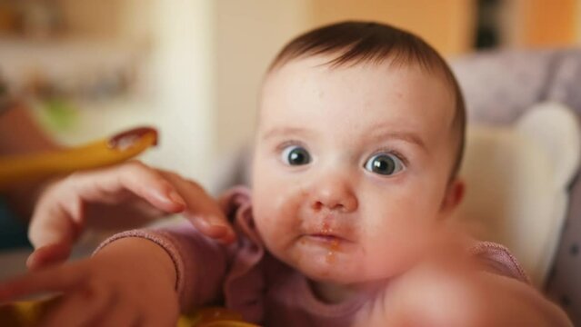 baby newborn eats. dirty mess baby girl eating vegetables. baby daughter eats on a feeding chair dirty face. naughty dirty babe indulges while feeding. happy kid dream family indoors weaning concept