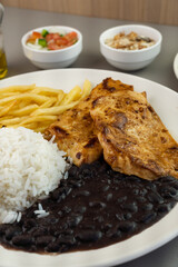 Delicious executive dish of chicken fillet, rice, beans, french fries and green salad with lettuce, tomato and onion accompanied by farofa and vinaigrette. Typical Brazilian food. Selective focus