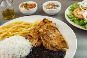 Delicious executive dish of chicken fillet, rice, beans, french fries and green salad with lettuce, tomato and onion accompanied by farofa and vinaigrette. Typical Brazilian food. Selective focus