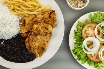 Delicious executive dish of chicken fillet, rice, beans, french fries and green salad with lettuce, tomato and onion accompanied by farofa and vinaigrette. Typical Brazilian food. Selective focus