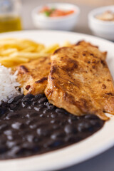 Delicious executive dish of chicken fillet, rice, beans, french fries and green salad with lettuce, tomato and onion accompanied by farofa and vinaigrette. Typical Brazilian food. Selective focus