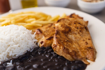 Delicious executive dish of chicken fillet, rice, beans, french fries and green salad with lettuce, tomato and onion accompanied by farofa and vinaigrette. Typical Brazilian food. Selective focus