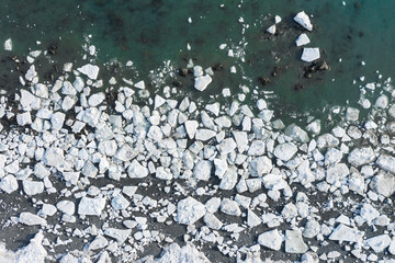 Aerial view of melting ice on the sea coast. Top view of white ice floes on the shore and in the water. Problems of climate change and global warming in the polar regions of the Earth. Northern nature