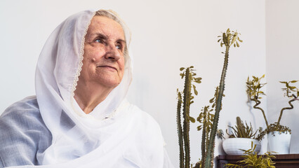 Portrait of old Muslim woman at eighties wearing white hijab sitting at home while fasting during...