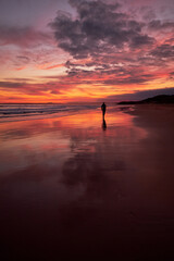 A beautiful vibrant sunset with stunning orange and red colours in the sky above the sea. With the silhouette of a person running along the beach in the distance.