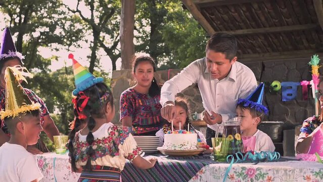  ¡Feliz cumpleaños! Familia celebrando un cumpleaños en el parque. Familia latina con sombreros de fiesta soplando velas en el pastel.