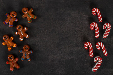 Cute Candy cookie in the form of a gingerbread man and his cane, covered with chocolate and colored icing sugar, on a wooden stick. Dark gray background. Top view. Copy space