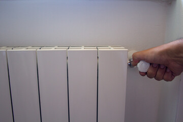 Image of a man's hand closing the knob of a radiator. Problem of the excessive cost of heating the...
