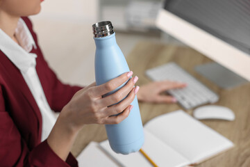 Woman holding thermos bottle at workplace, closeup.