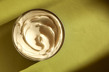 Jar of face cream on green background, top view. Space for text