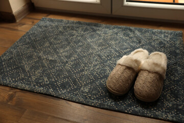 Stylish door mat and slippers on wooden floor indoors