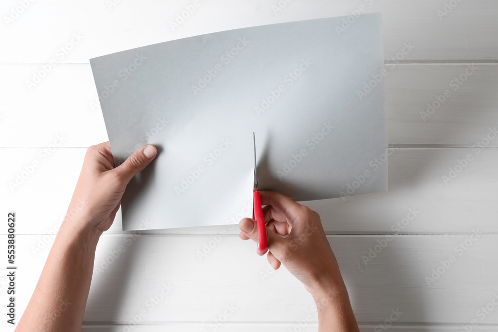 Wall mural Woman cutting paper with scissors at white wooden background, top view