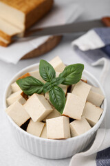 Bowl of smoked tofu cubes with basil on white table, closeup