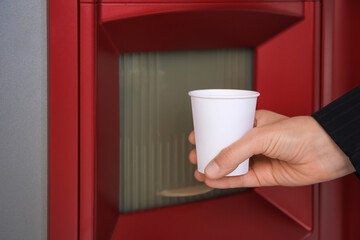 Woman taking paper cup with coffee from vending machine, closeup