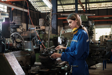 An industrial worker in protective and safety uniform and hardhat, young Caucasian female engineer works with metalwork machine in manufacturing factory. Professional production mechanical occupation.