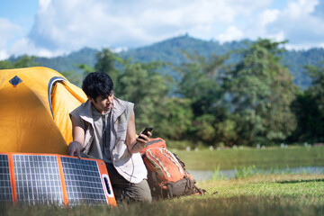Man at campsite charging gadgets with portable solar panel, modern technology for travel, Alternative electricity source, looking at smart phone