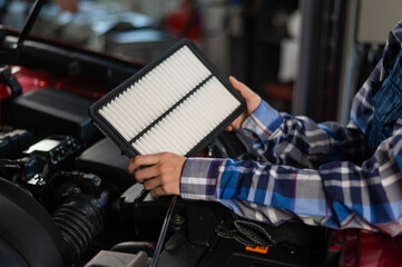 Caucasian female auto mechanic changes the engine air filter in the car.