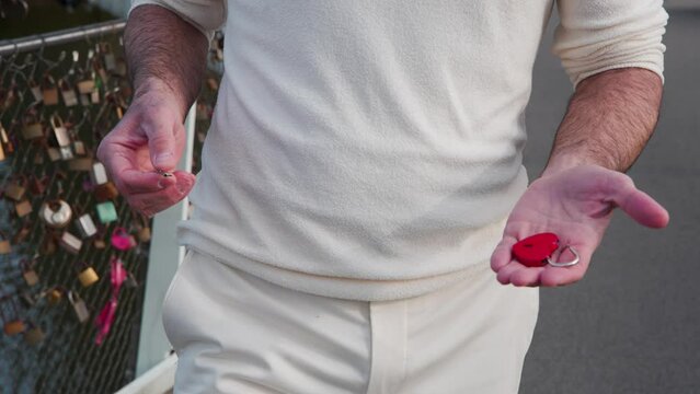 Man carrying red heart padlock and key to put on lock bridge fence.