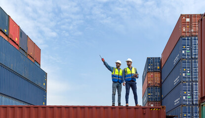 Shipment worker use a walkietalkie to point to container storage location, explain to colleague...