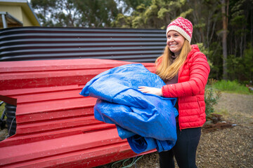 woman folding up a tarp at a campground in australia. camping tant and tarp while caravaning and camping in australia