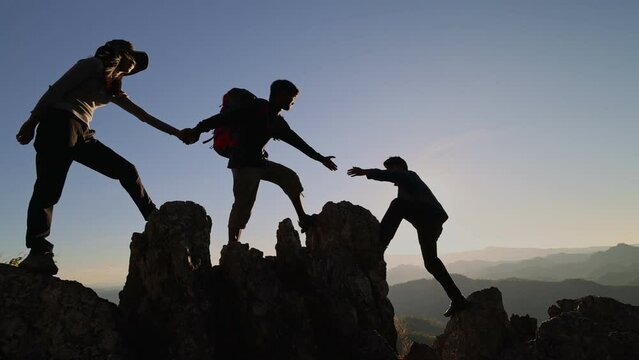 Silhouette of Group team tourists lends helping hand climb cliffs mountains helping hand. teamwork people climbers climb top overcoming hardships, teamwork helping hand business travel  concept.